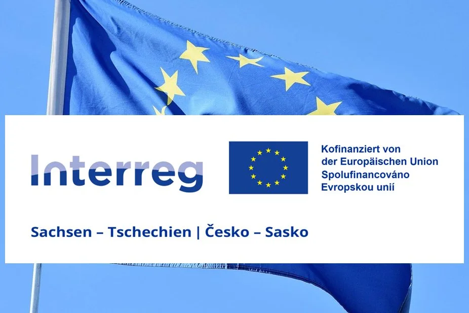 EU-Flagge im Wind, darüber das INTERREG Sachsen-Tschechien-Logo