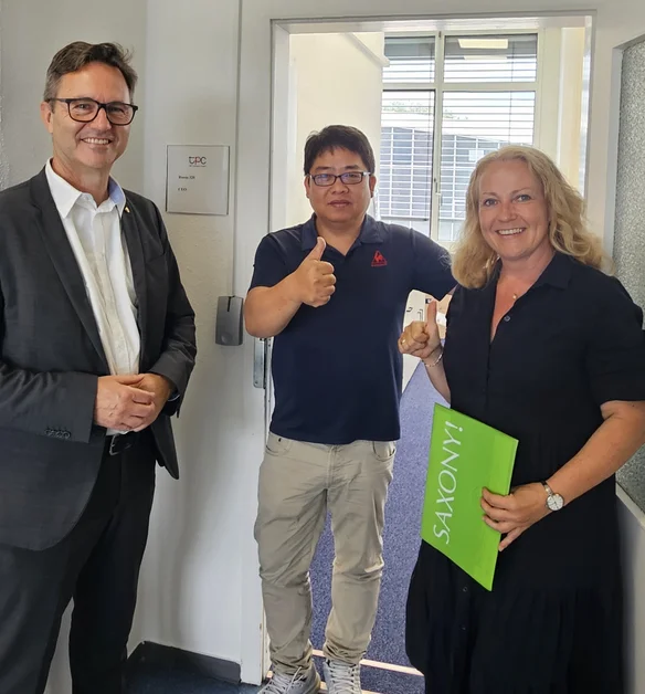 WFS-Geschäftsführer Thomas Horn und Cornelia Probst, Mitarbeiterin im Bereich Investorenservice bei der WFS, gratulieren dem Geschäftsführer von TPC Germany GmbH, West Tu, zum ersten Geburtstag der Firma am Standort Dresden.
